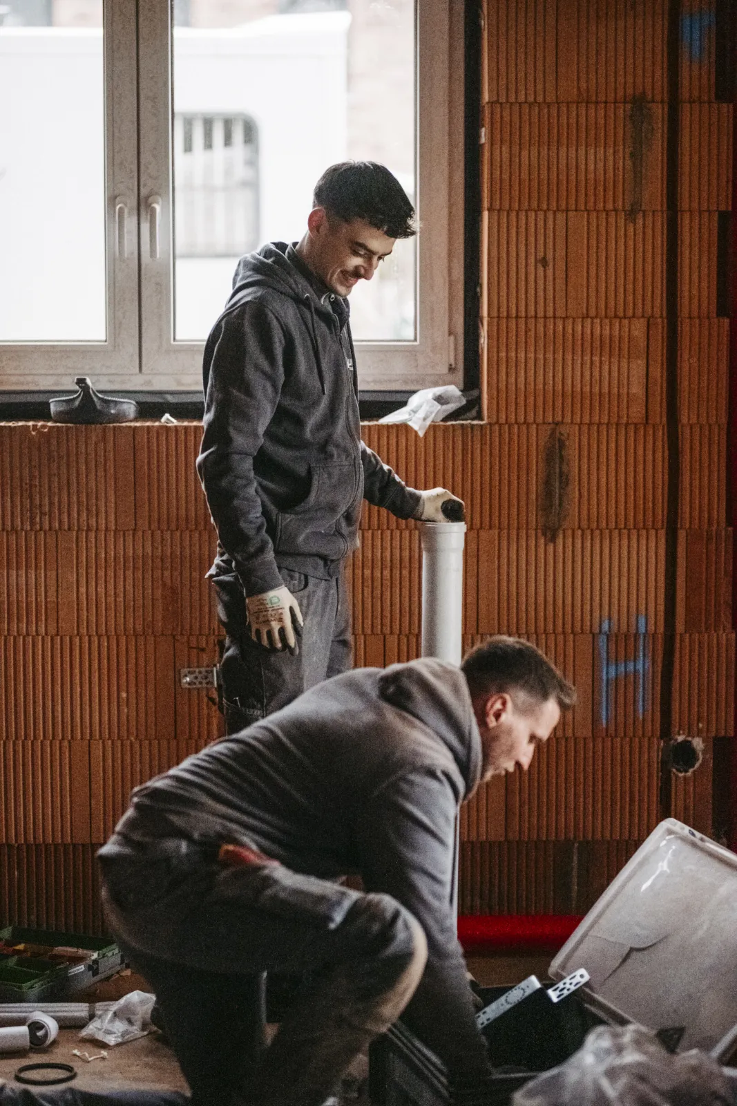 Zwei Monteure bei der Arbeit im Rohbau vor einer Ziegelwand