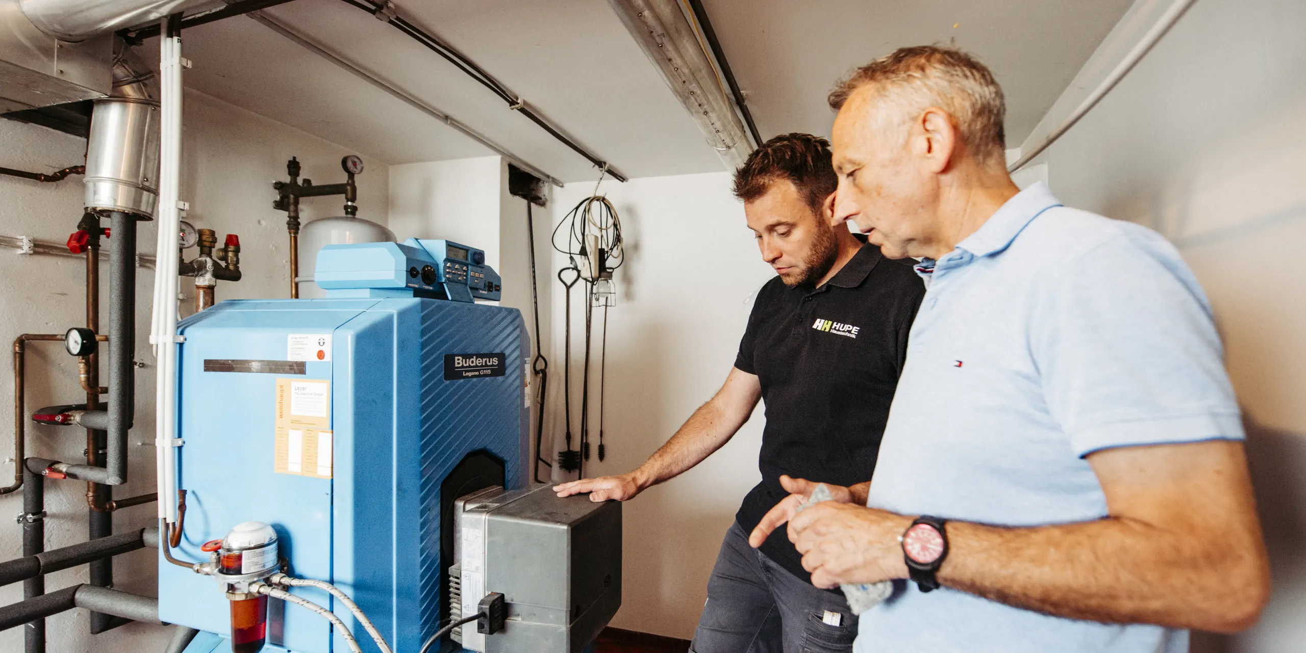 Mitarbeiter von Hupe Haustechnik bespricht mit einem Kunden den alten Ölkessel im Heizungskeller